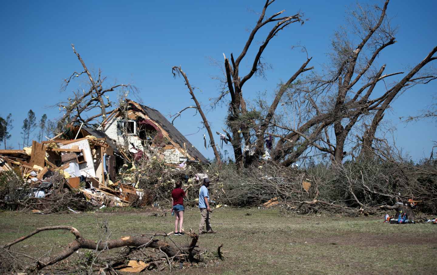 People looking at a destroyed home with trees