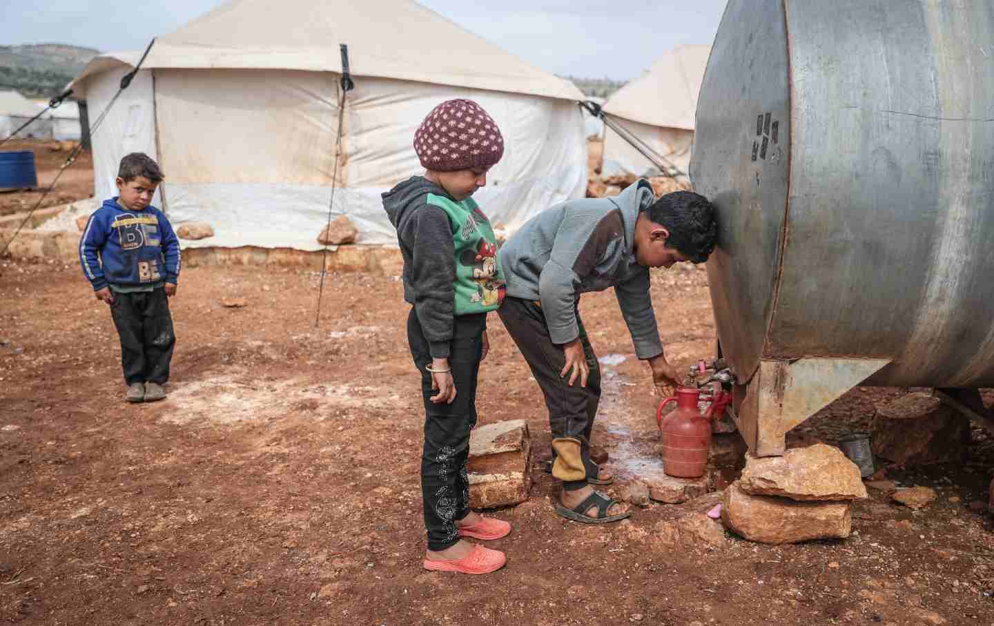Syrian children draw from a water container at a refugee camp in the village of Kafr Aruq.