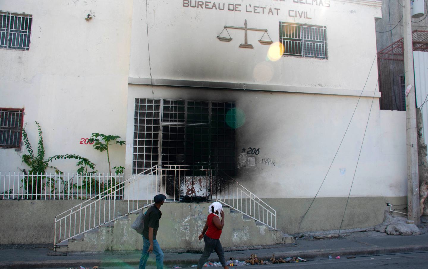 2024 年 3 月 6 日，海地太子港，前一天，人们走过被武装团伙纵火焚烧的法庭。3 月 4 日，海地首都基本被关闭，当局在一次袭击后实施了紧急状态一座监狱释放了数千名囚犯。