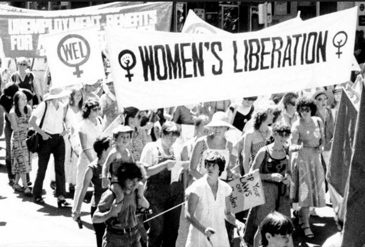 Heather Booth, in white at the bottom, pushing a stroller, participates in a Women’s Liberation March around 1970.