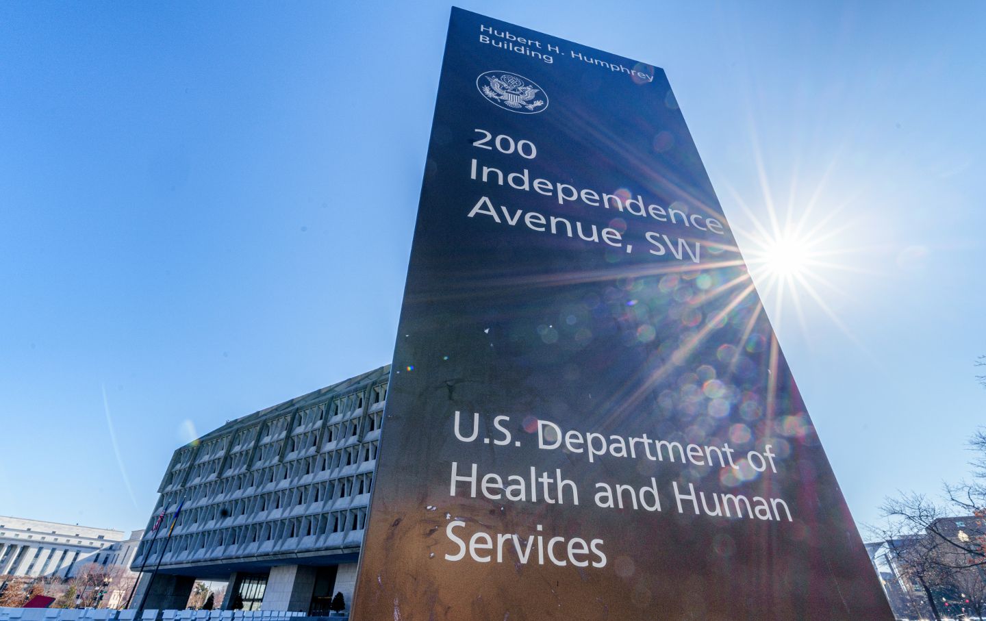 Looking up at the sign outside the Department of Health and Human Services building, against a sunny sky.