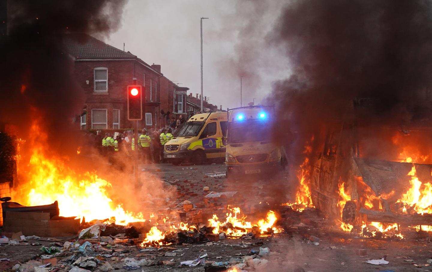 Riot police hold back anti-immigrant protesters near a burning police vehicle in Southport, England.