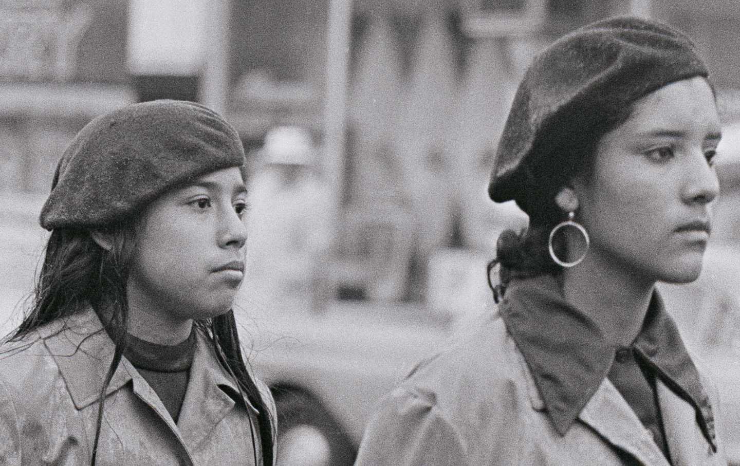 Two women stand in uniform with their hands behind their back.