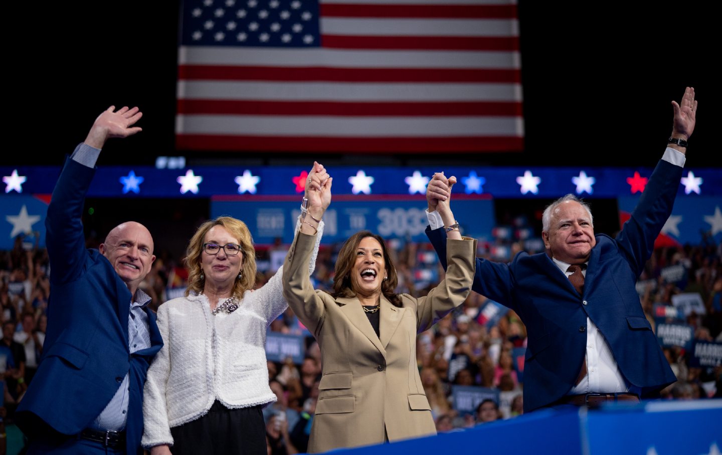 Kamala Harris and Tim Walz smiling and raising their hands at a rally.