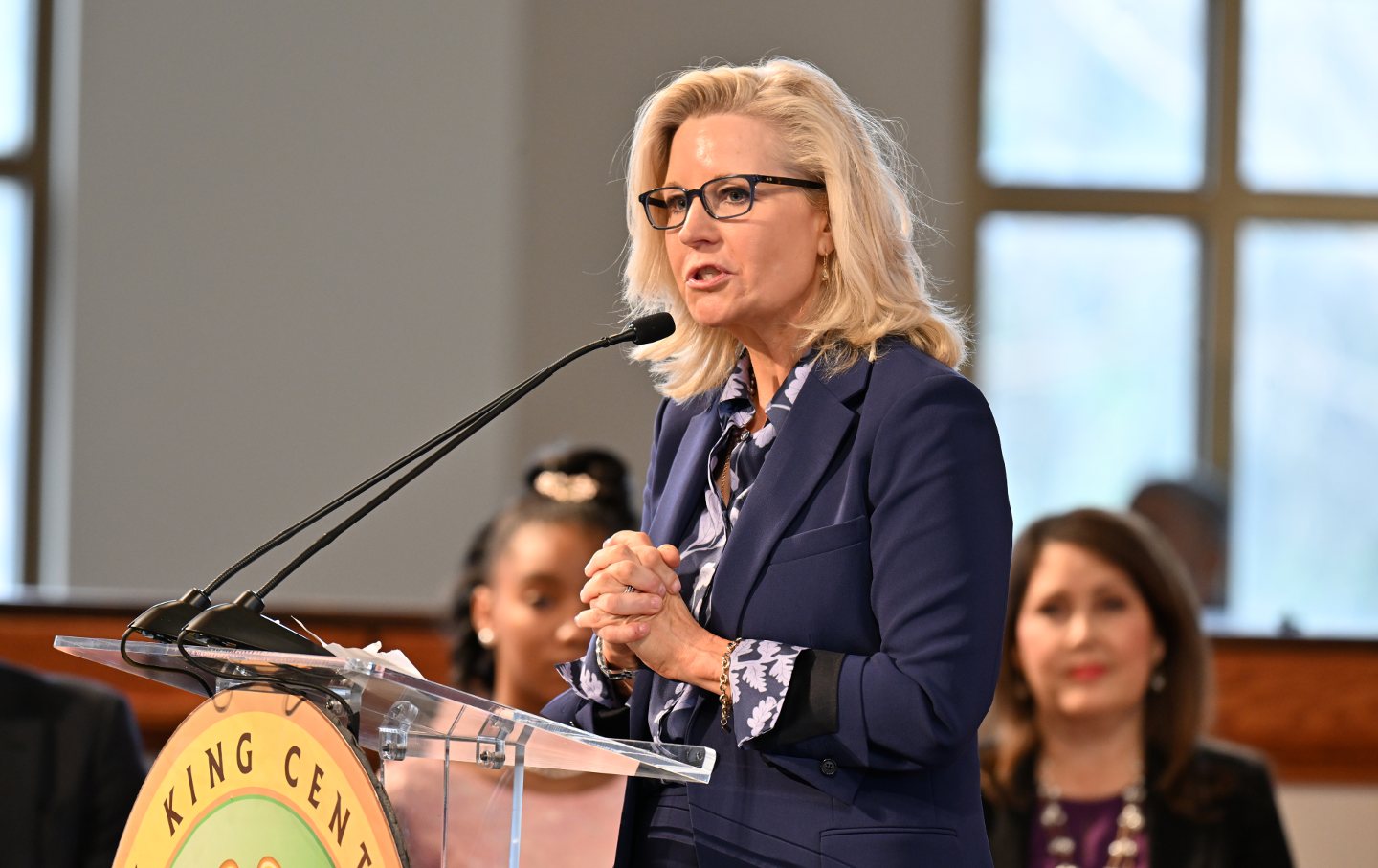 Liz Cheney looking intently, speaking at a podium that reads "King Center."