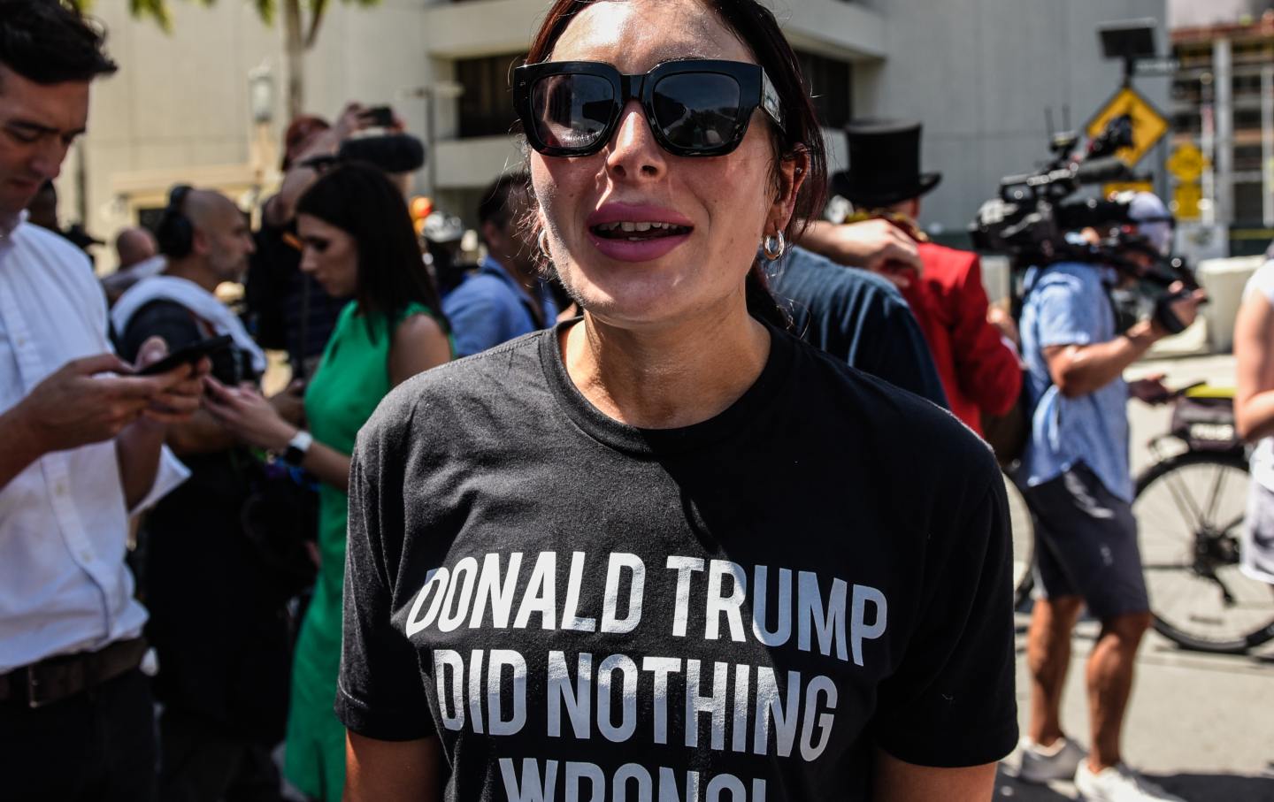 Laura Loomer, in large sunglasses, stands in front of a courthouse wearing a shirt that reads "Donald Trump did nothing wrong."