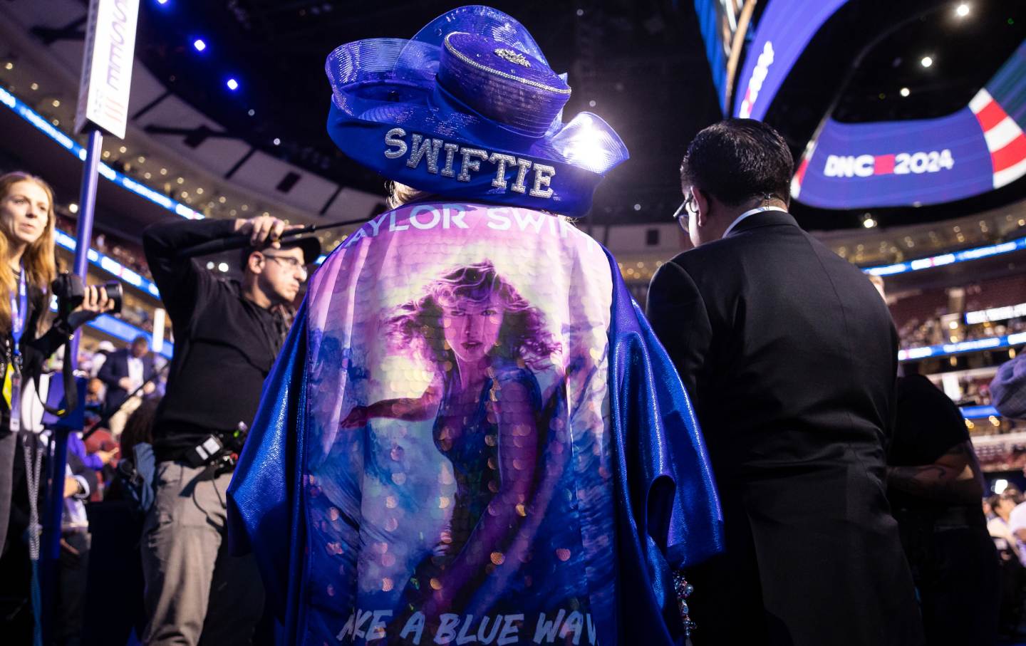 A photo of a Taylor Swift fan on the floor at the Democratic National Convention wearing a "Swiftie" hat and an image of Taylor Swift on her shirt.