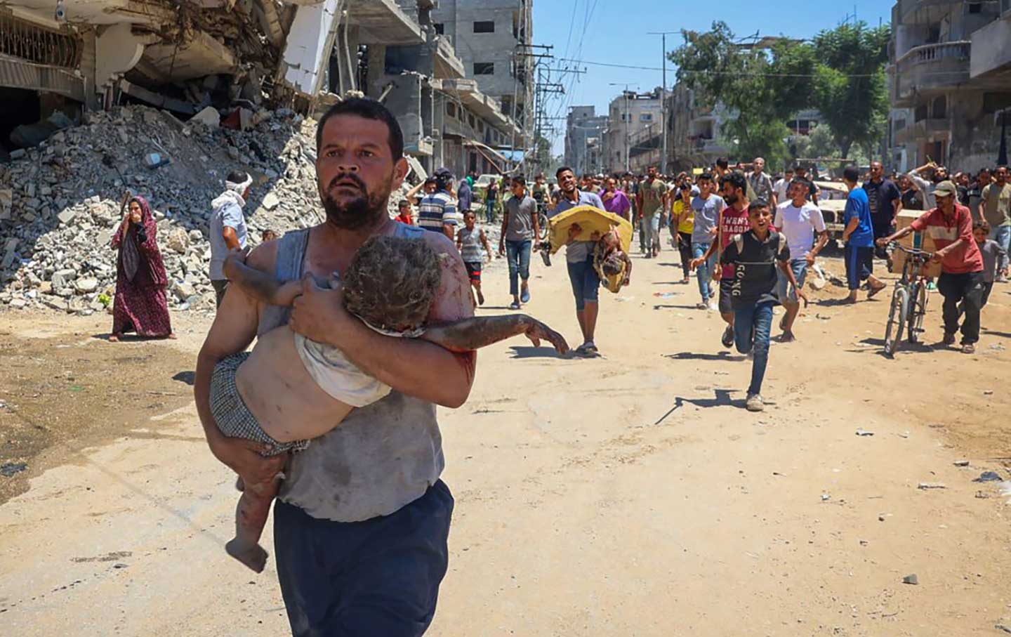 A man carries an injured child, fleeing down a road in al-Bureij refugee camp in the central Gaza Strip.