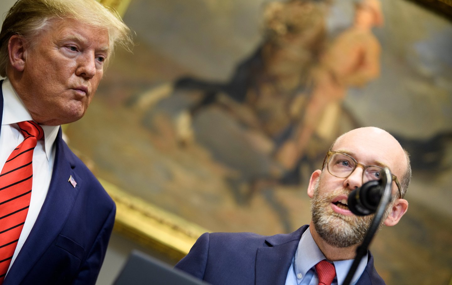 Former president Donald Trump on the left with Russell Vought on the right, at a podium.