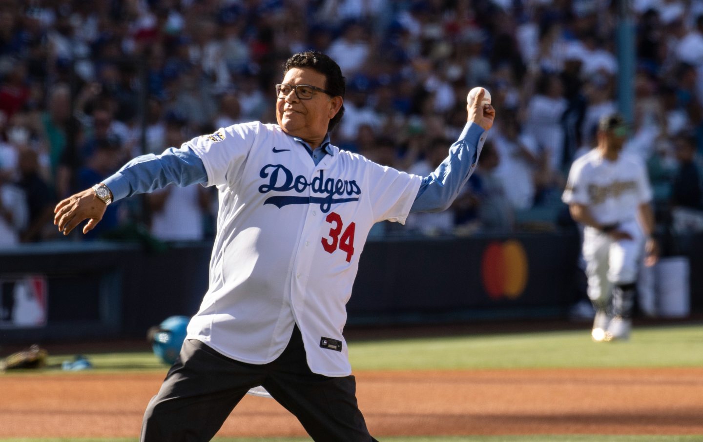 Fernando Valenzuela, in his old Dodgers jersey, throws the pitch in a baseball field.