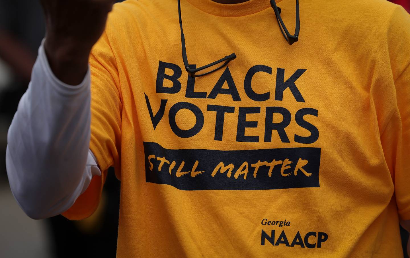 A close-up of a yellow t-shirt reading "Black Voters Still Matter" worn by a voter.