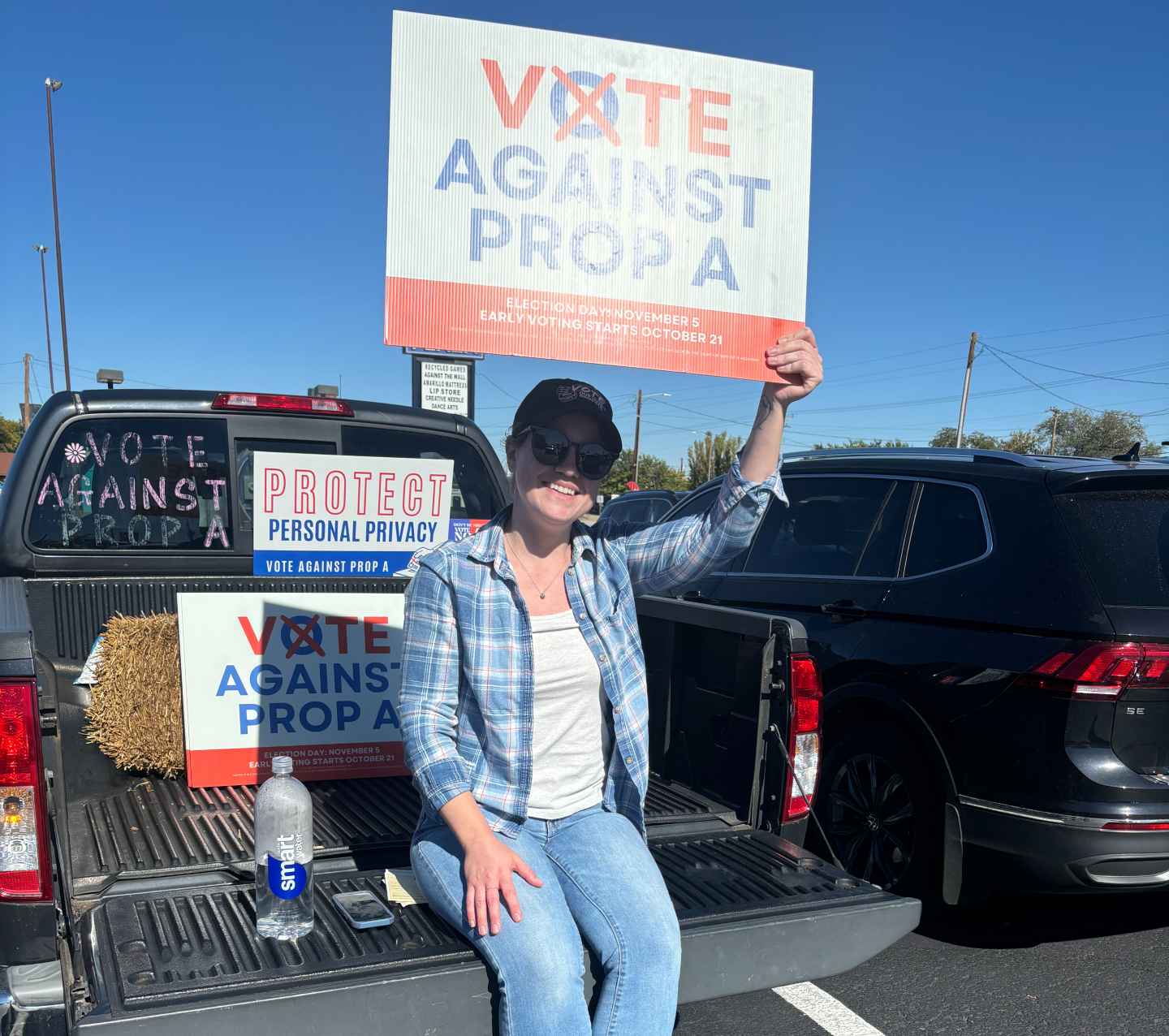 Abortion-rights activist Harper Metcalf hods up a sign reading "Vote Against Prop A" and "Protect Personal Privacy" while sitting in the bed of a truck.