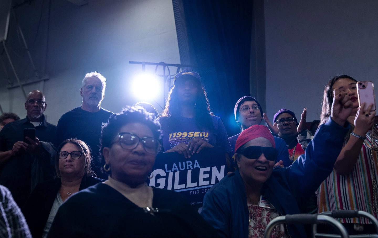 A low-light photo of supporters facing a rally. One holds a 