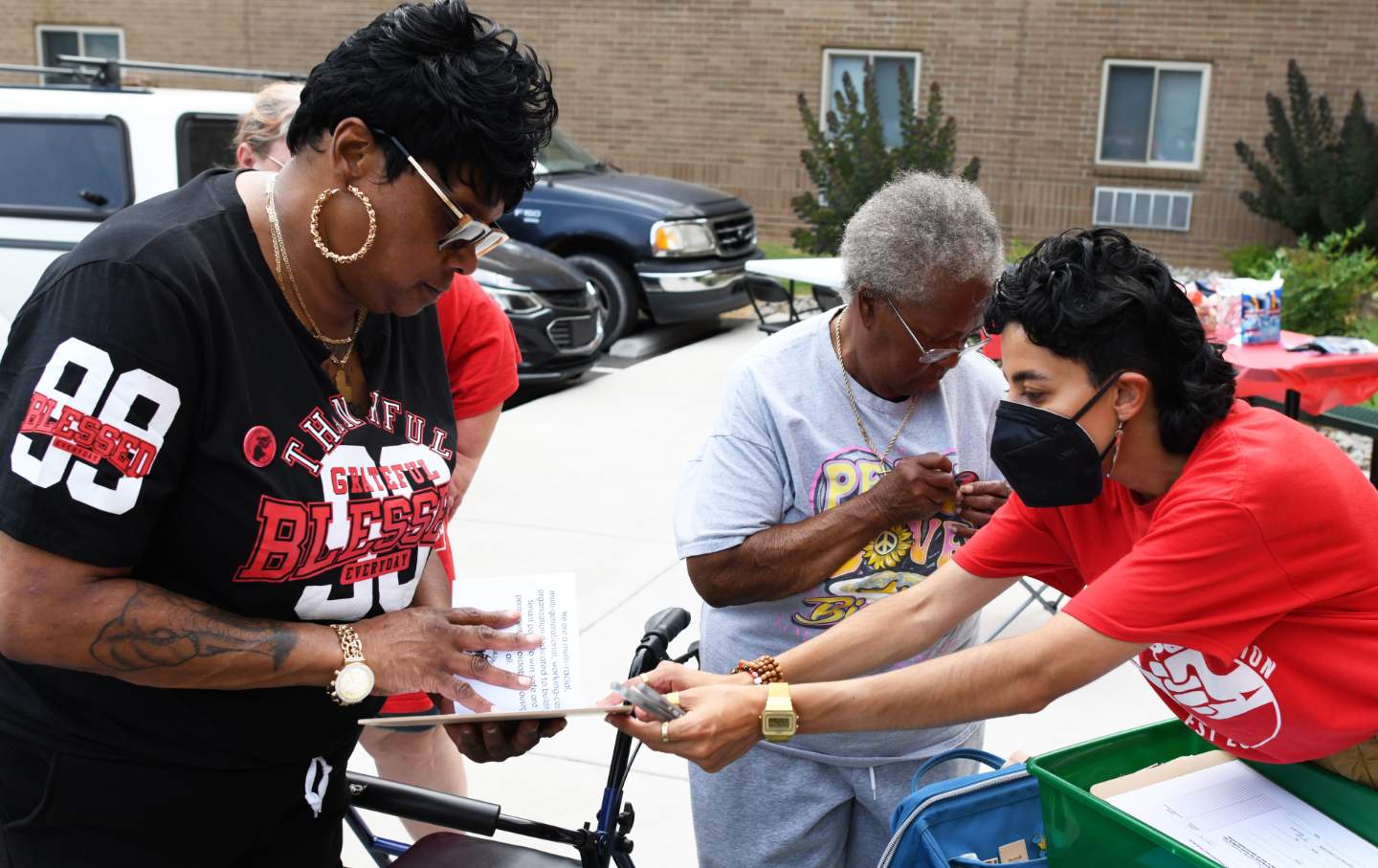 Three people in a parking lot outside a residential building look at and sign tenant union cards and materials.