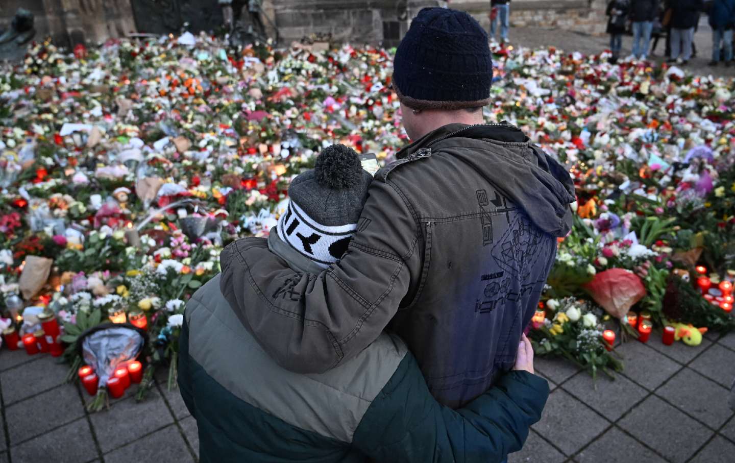 Los dolientes se abrazan frente a un monumento improvisado de flores y velas para las víctimas de un ataque de un coche con caballos en un mercado navideño en Magdeburgo, este de Alemania, el 23 de diciembre de 2024.