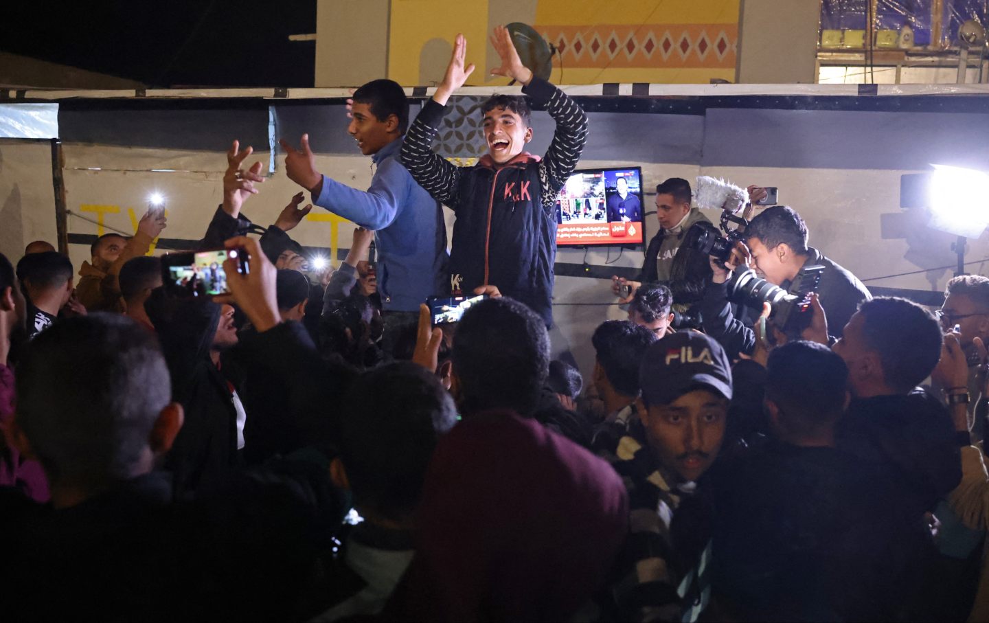 People celebrate while watching a television along a street in Khan Yunis in the southern Gaza Strip on January 15, 2025.