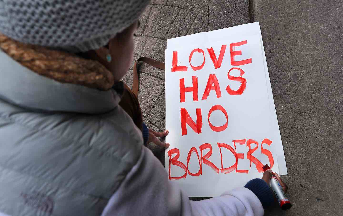 Tori Furtado, from Boston, kneels down to write a sign that reads, “Love has no borders,” in front of the Chinatown Gate, where hundreds gathered for a rally before marching to the State House in a demonstration against President Trump’s new immigration order the day after it was issued, January 28, 2017.