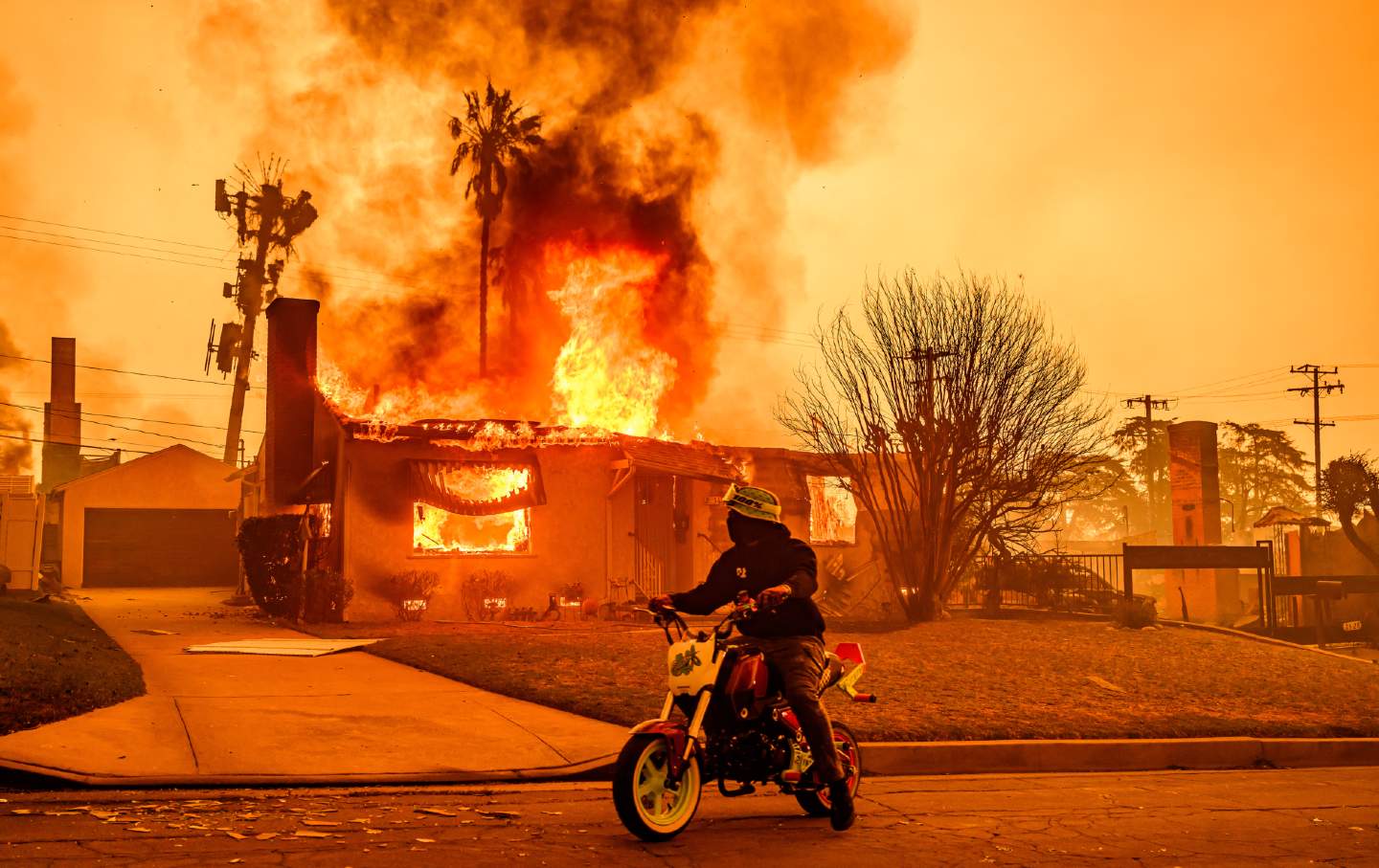 A motorcyclist stops to look at a burning home during the Eaton fire in the Altadena area of Los Angeles County, California, on January 8, 2025.