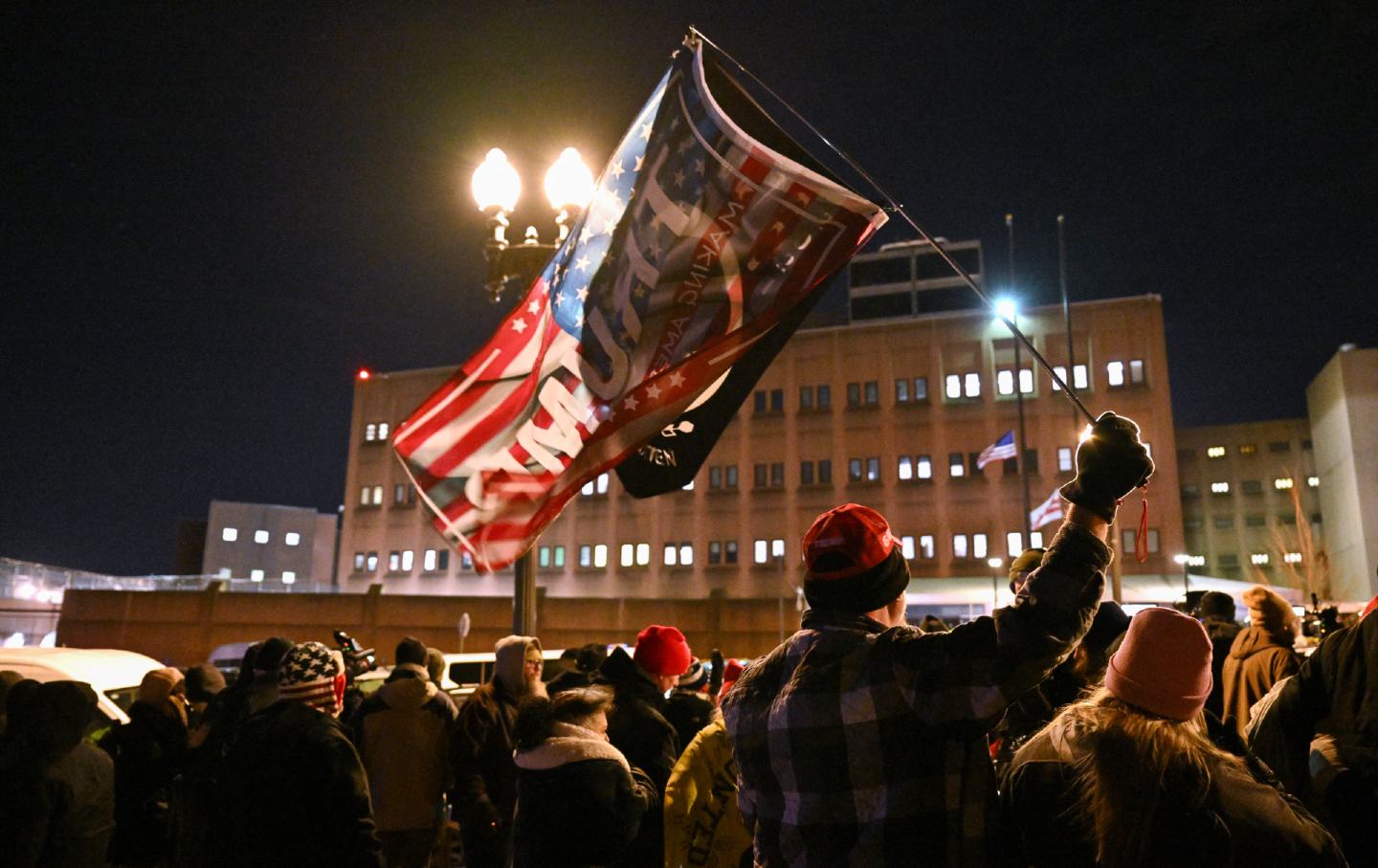 Seseorang mengibarkan bendera Trump saat keluarga dan teman dari peserta kerusuhan 6 Januari 2021 yang dipenjara di US Capitol, menunggu di luar Fasilitas Penahanan Pusat DC di Washington, DC, pada 20 Januari 2025.