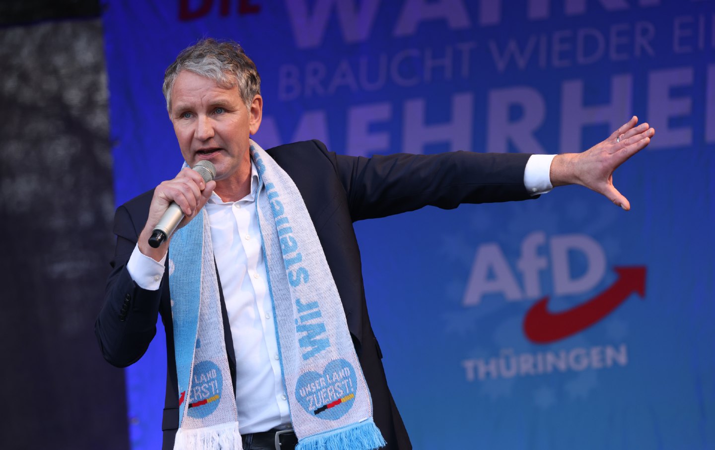 Man with a microphone stands onstage as he speaks.