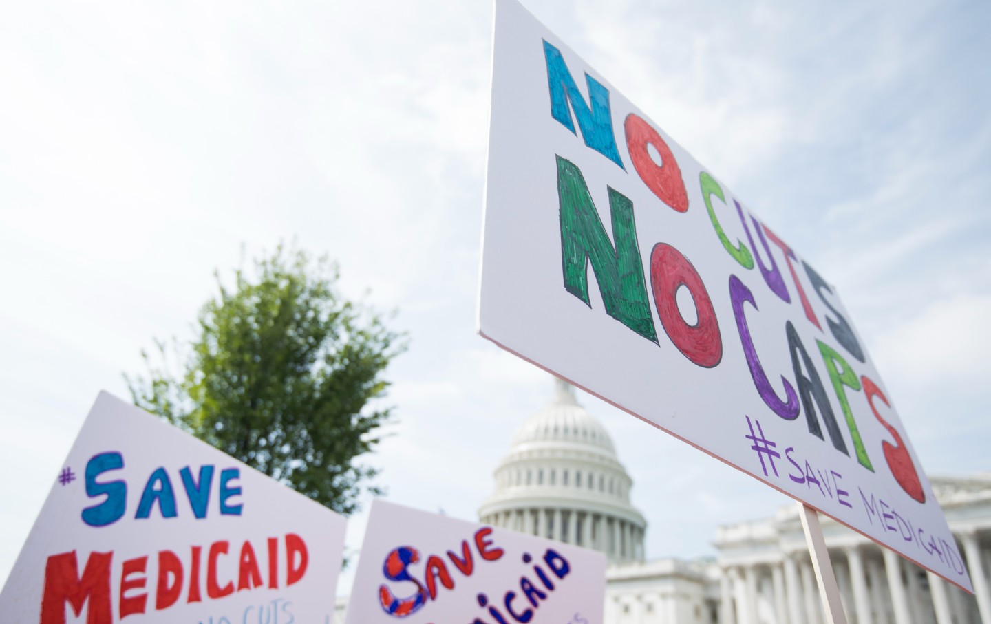 People hold up signs that read "Save Medicaid" and "No cuts, no caps"