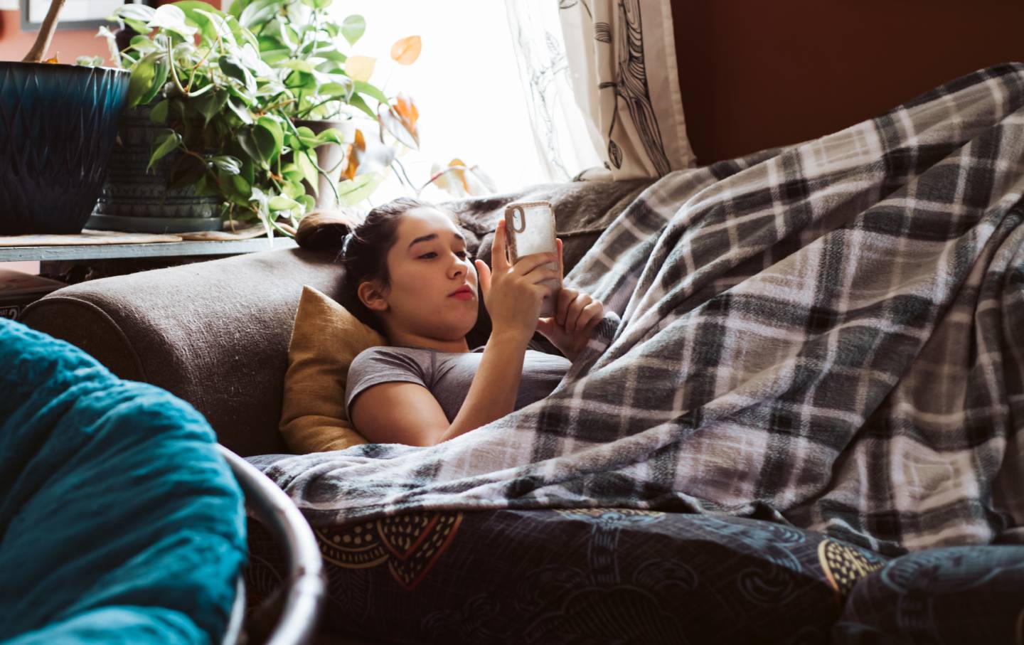 A teenager lying on a couch watching something on their phone.