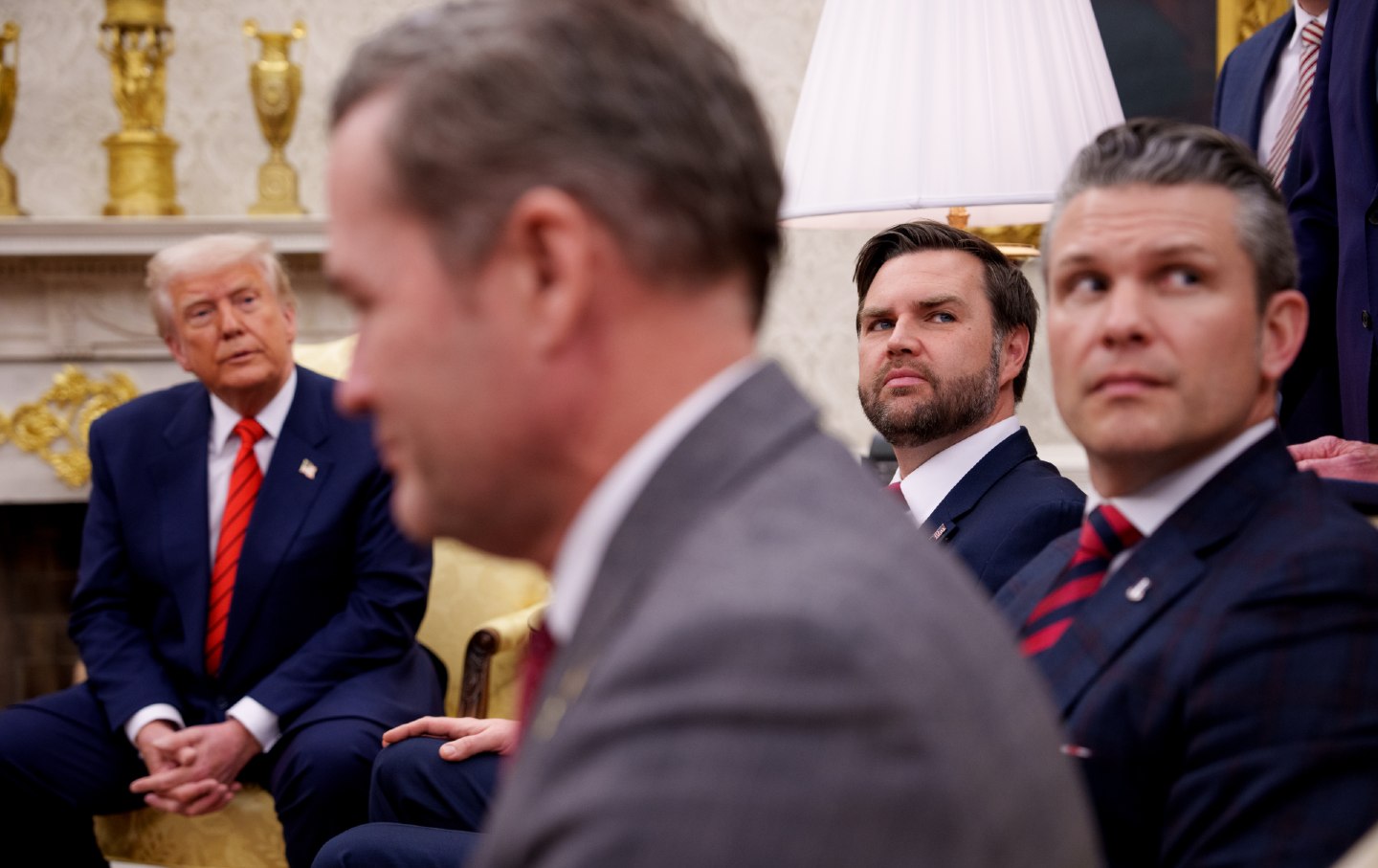 Four men in suits sit in the Oval Office.